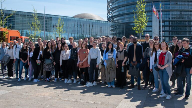 Die Gruppe Absolvent*innen, Studierender und internationaler Gäste beim Gruppenfoto vor dem Europäischen Parlament in Straßburg